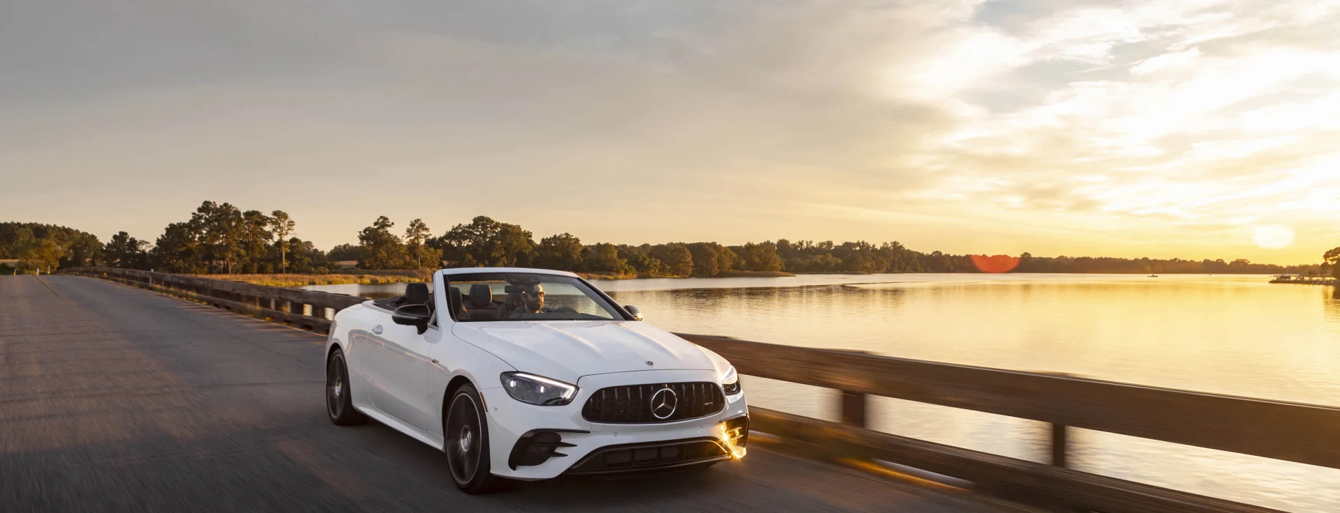 A white Mercedes-AMG E-Class Cabriolet driving across a lakeside bridge at sunset, from Mercedes-Benz of Fort Walton Beach, 1000 Beal Parkway NW, Florida