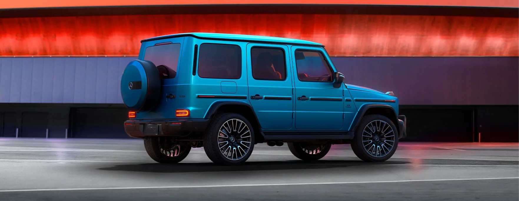 2027 Mercedes-AMG G 63 in blue, rear three-quarter view against a red-lit backdrop