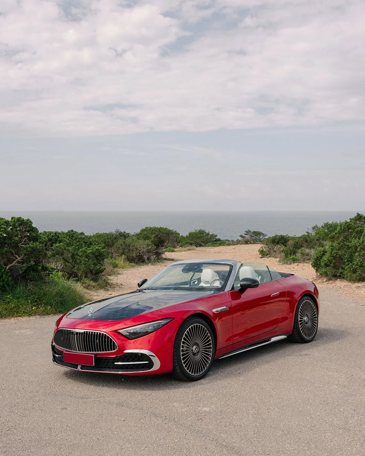 Red Mercedes-Maybach SL 680 roadster with the top down, parked on a coastal road overlooking the sea, showing the Maybach grille and monogram hood