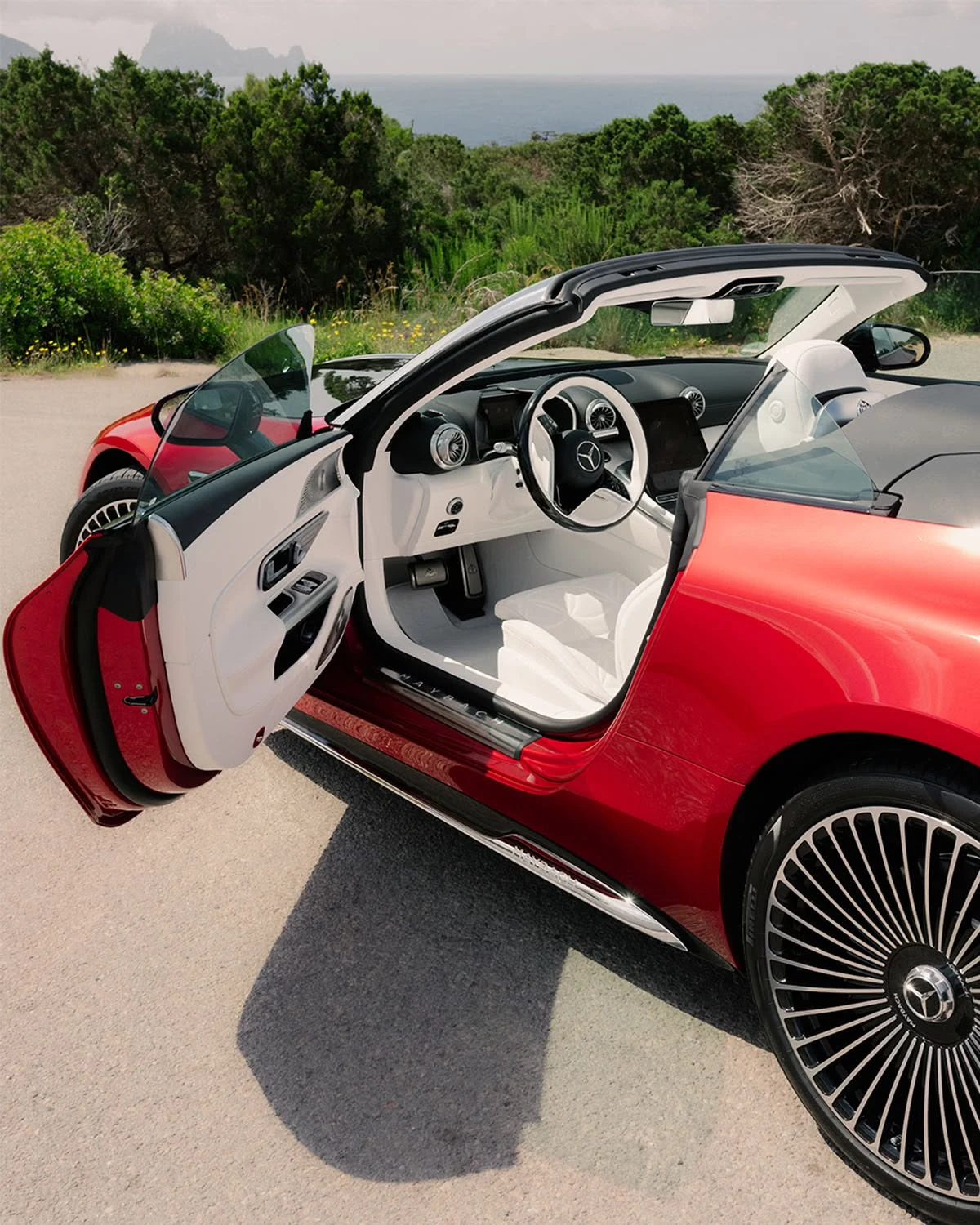 Red Mercedes-Maybach SL 680 with the door open, showing the white Nappa leather interior and the MAYBACH door sill, on a coastal road