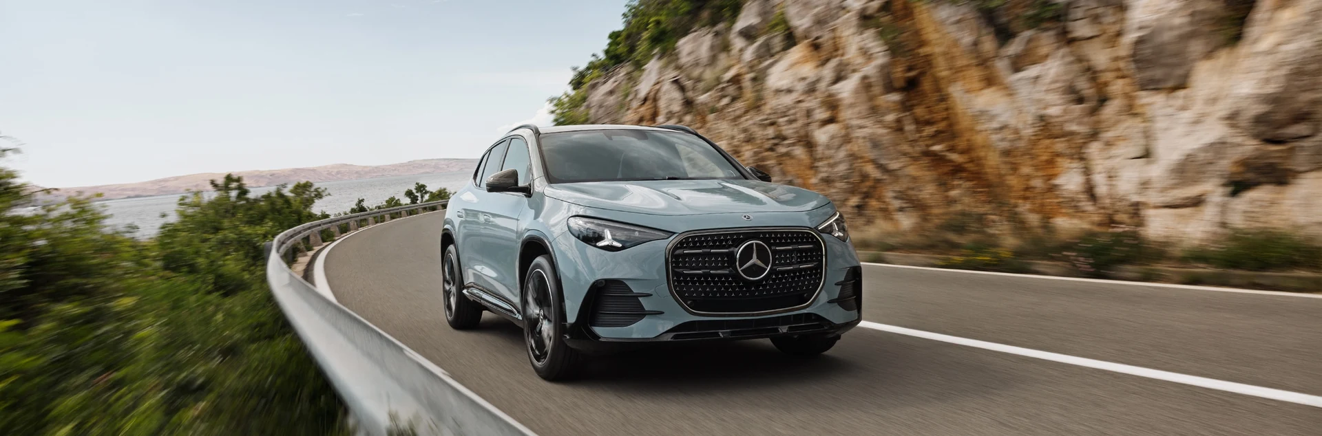 A Mercedes-Benz GLA SUV in light blue on a coastal road beside a rock face