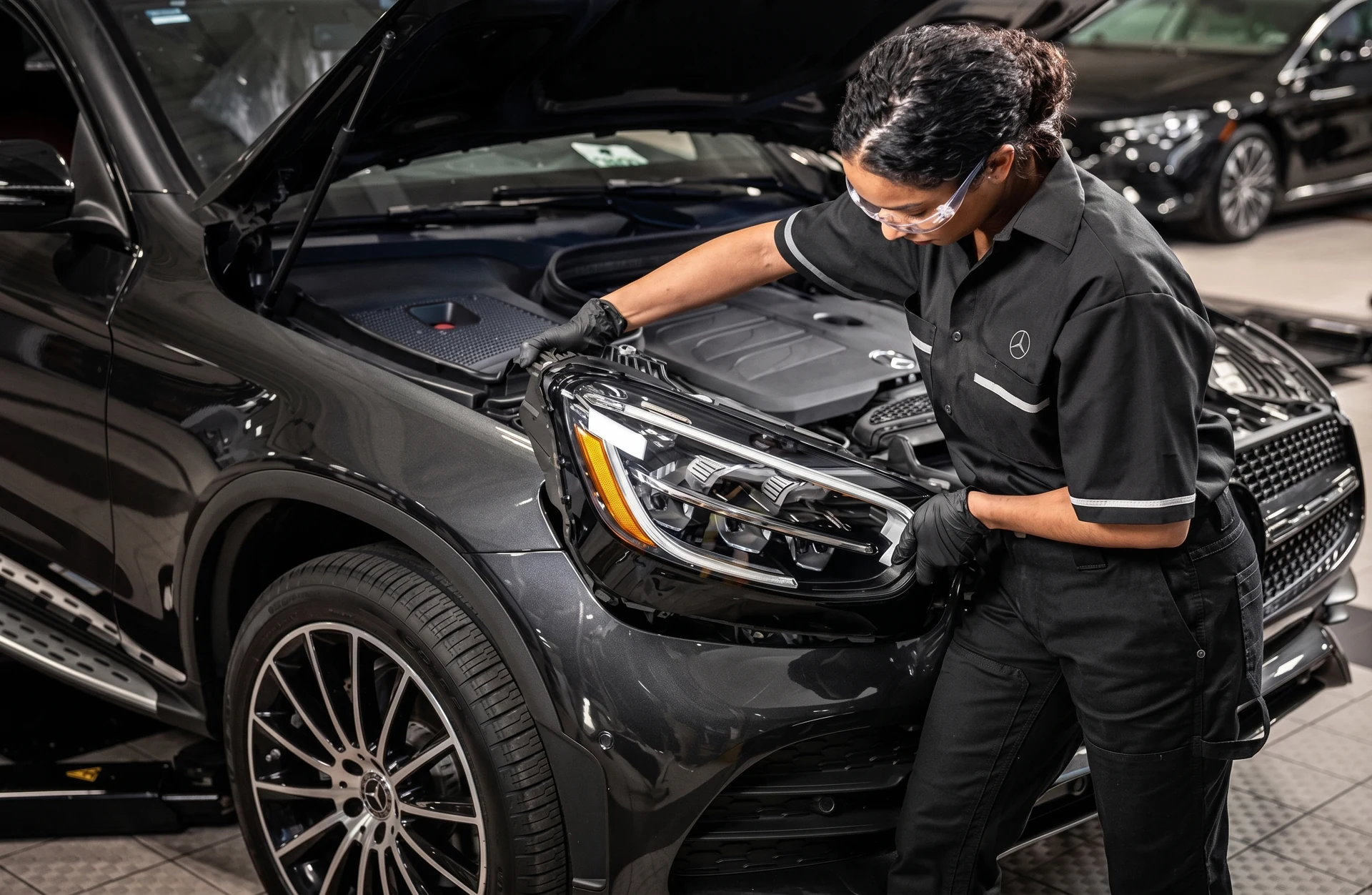 A Mercedes-Benz technician in safety glasses checking under the hood of a GLC in the workshop