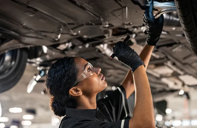 A Mercedes-Benz technician inspecting the underbody of a raised car with a flashlight